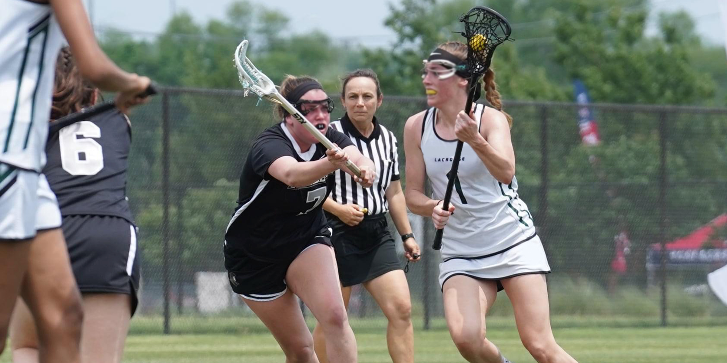 photo of two female lacrosse players going for the ball while a lacrosse official watches the space between the players for a foul