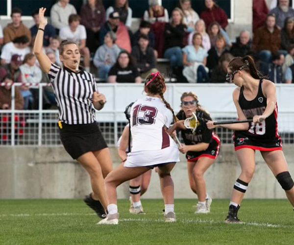 photo of a lacrosse official backing up after setting the draw in a girls' lacrosse game